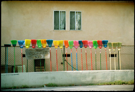 Photograph of brooms for sale along a fence